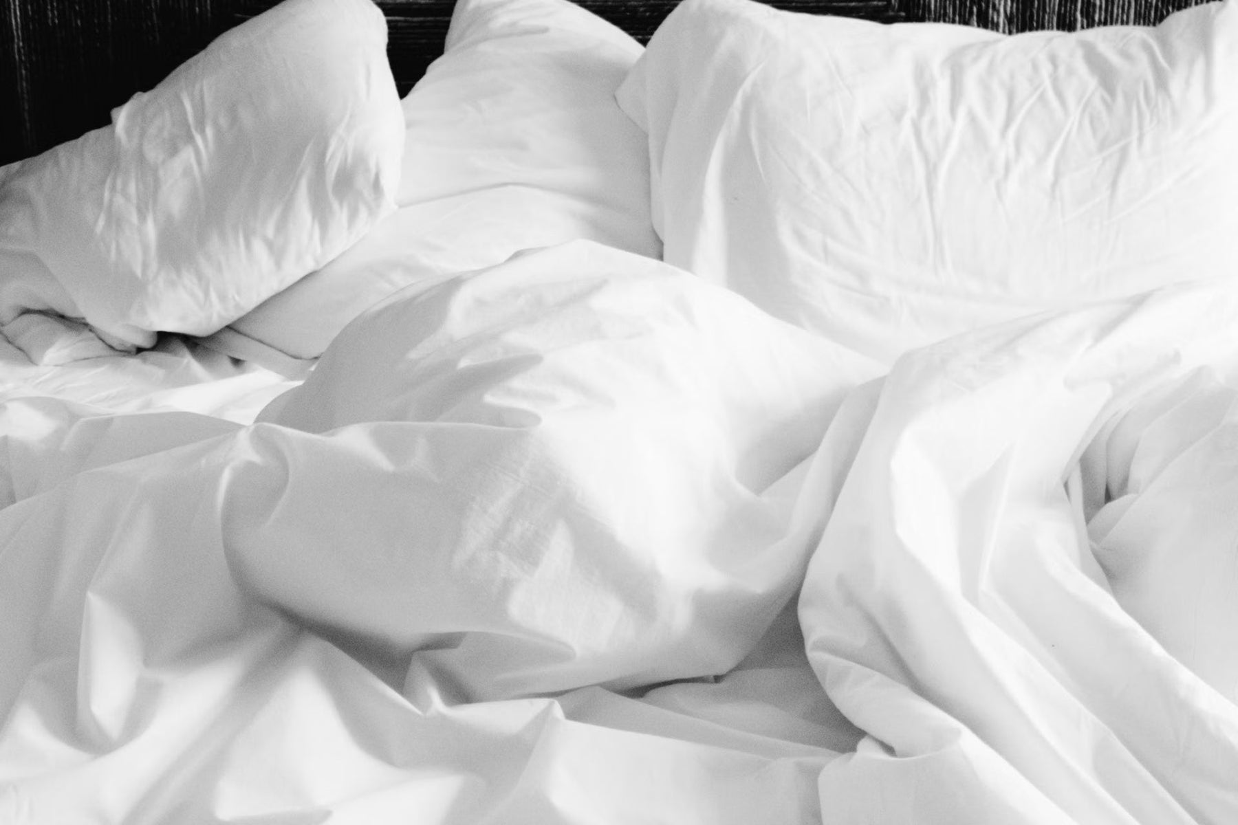 White bedsheets and pillows tossed together on bed, viewed up close.
